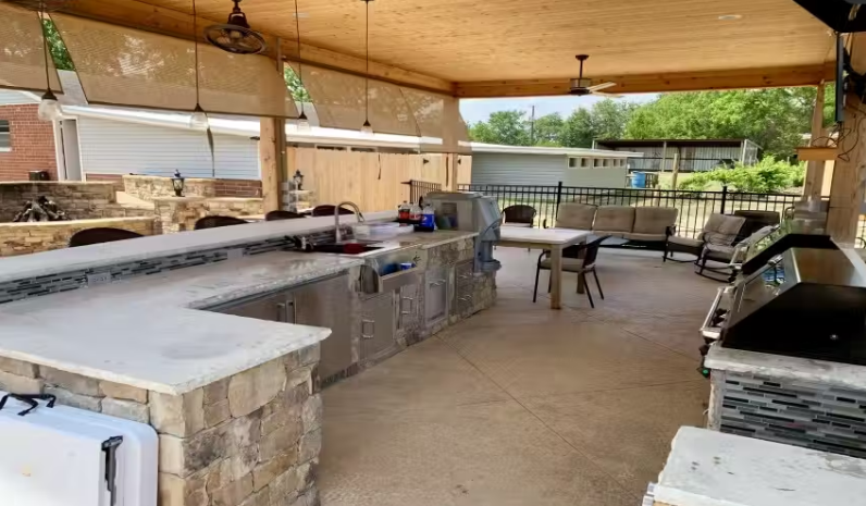 A large outdoor kitchen with a covered patio and a table and chairs.