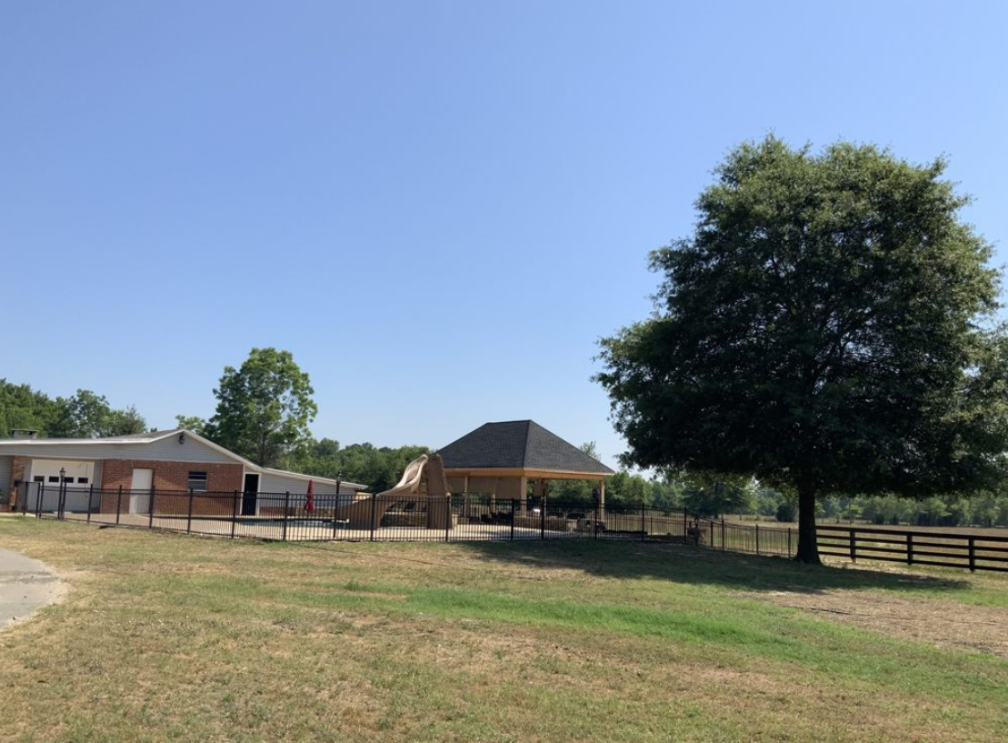 A large grassy field with a house in the background and a tree in the foreground.