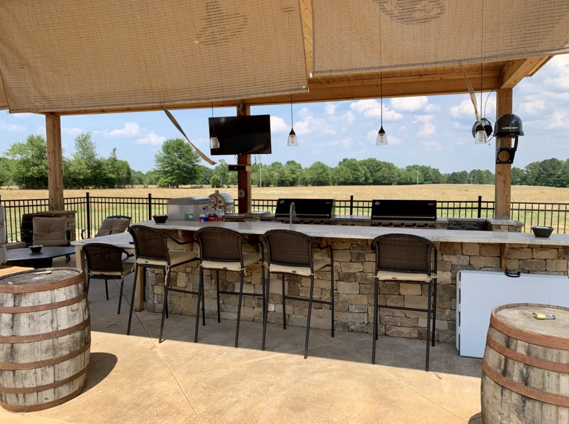 A patio with a bar , chairs , barrels and a television.