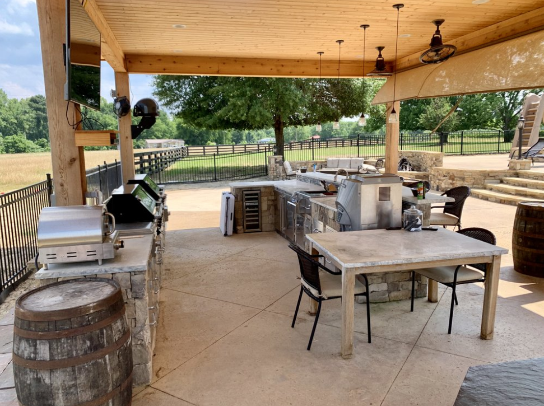 A large outdoor kitchen with a table and chairs and a grill.