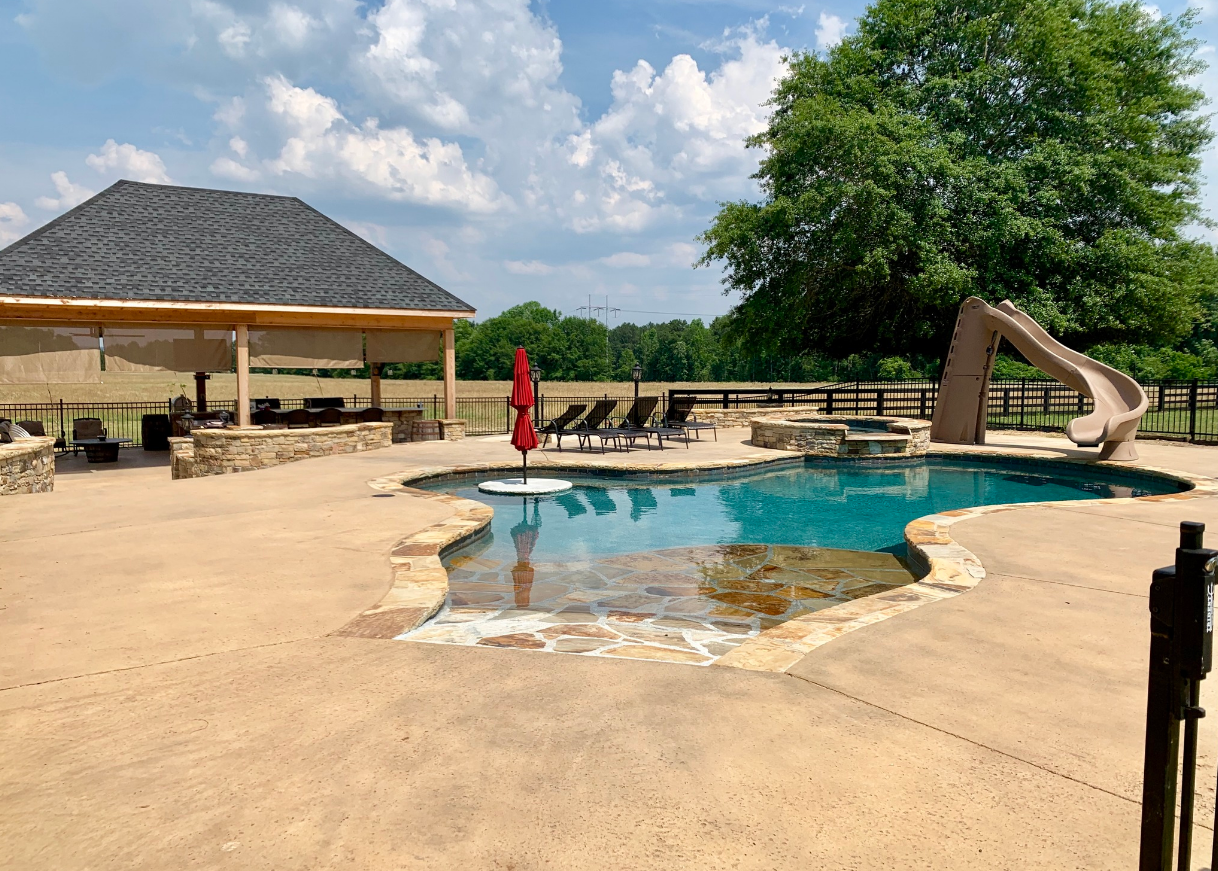 A large swimming pool with a slide and a gazebo in the background.