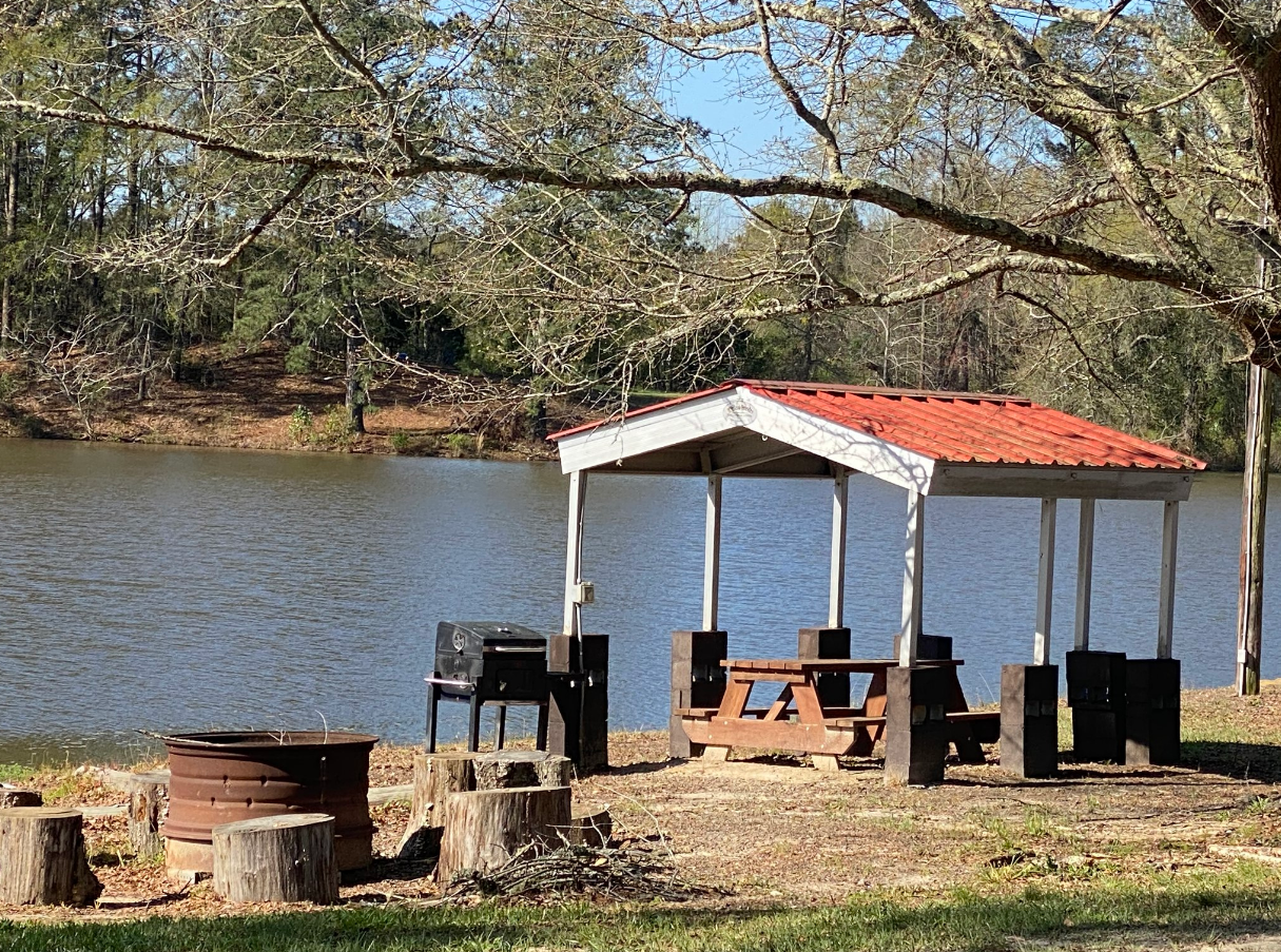 A covered area with a picnic table and chairs next to a lake.