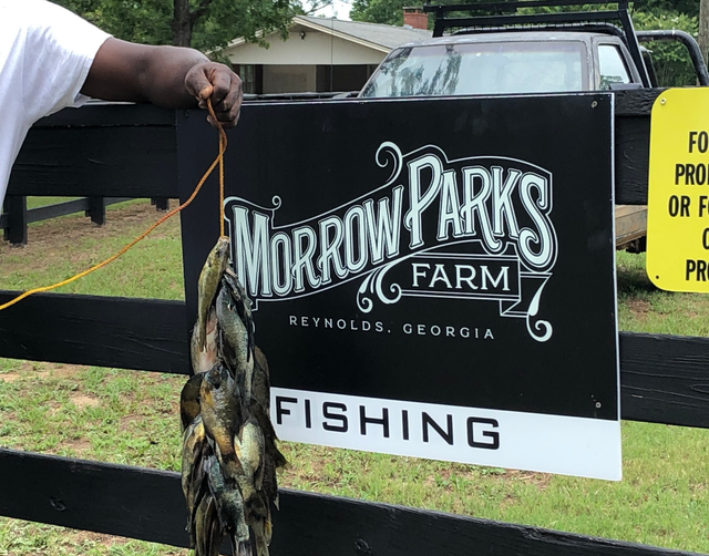 A man is holding a fish in front of a morrow parks farm fishing sign