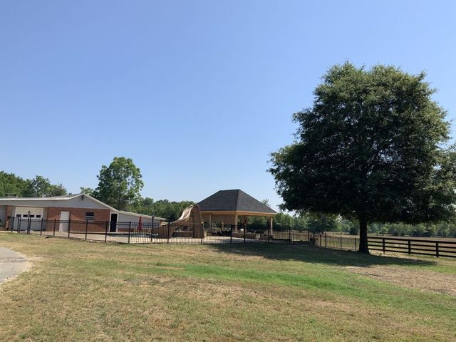 A large grassy field with a house in the background and a tree in the foreground.