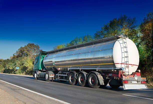 Un camión cisterna verde circula por una autopista, transportando líquido. El cielo azul brillaba.