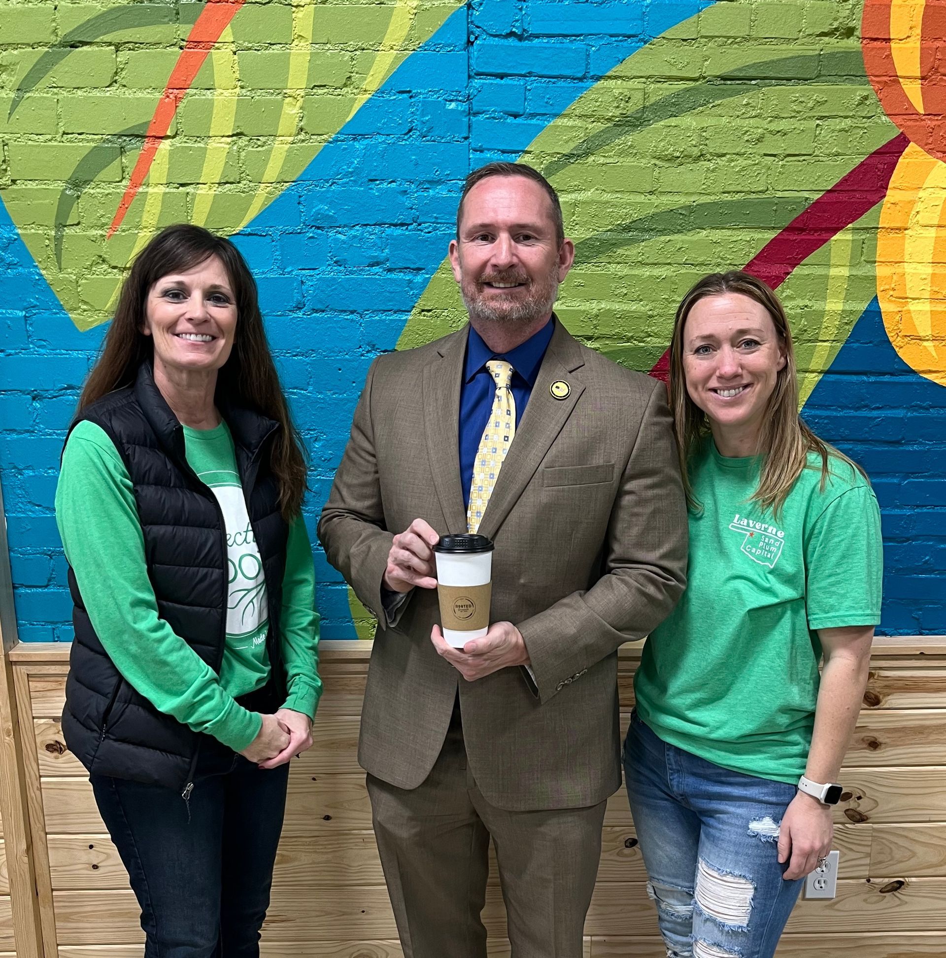 A man in a suit is holding a cup of coffee while standing next to two women.