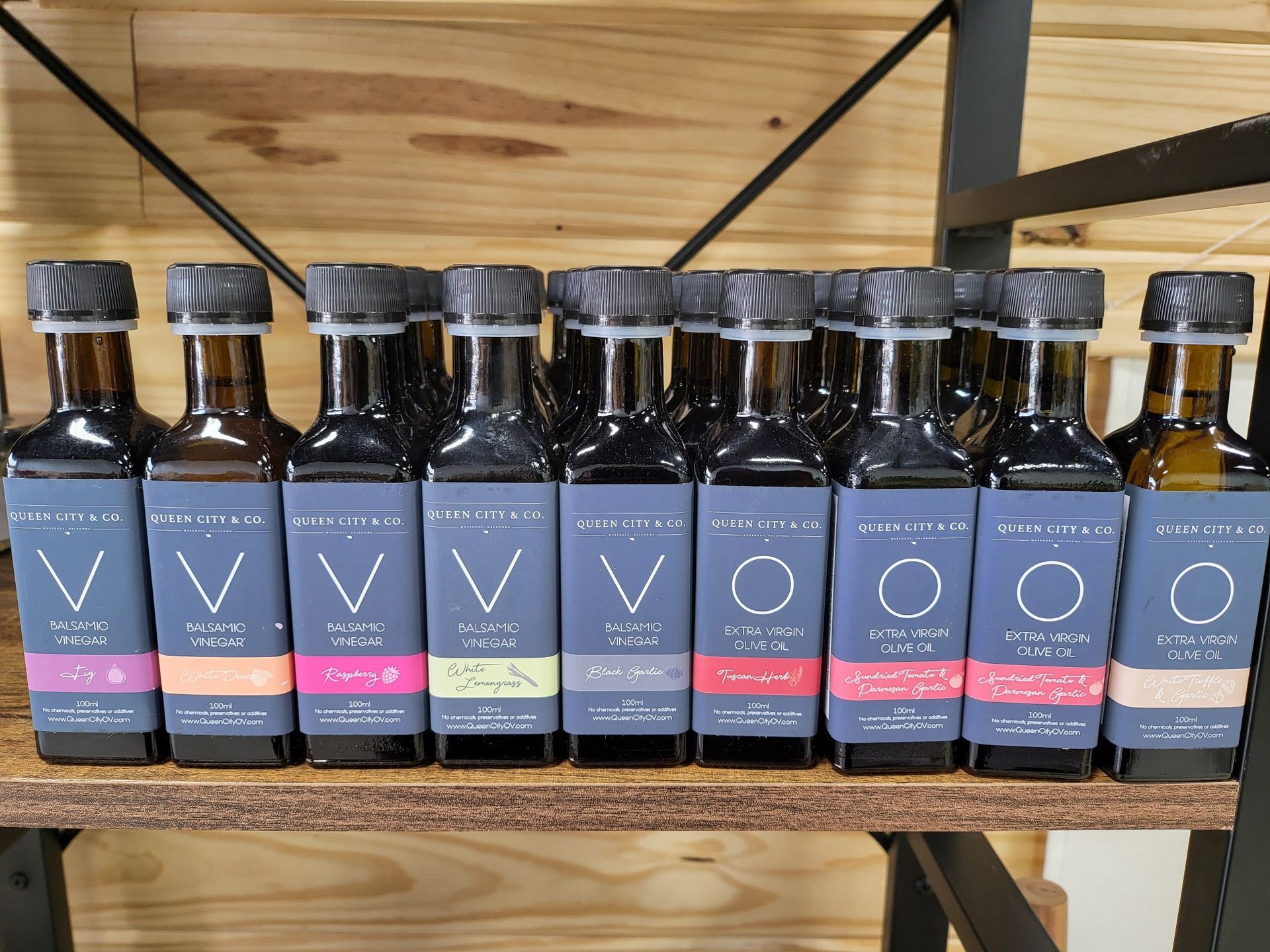 A row of bottles of olive oil are lined up on a wooden shelf.
