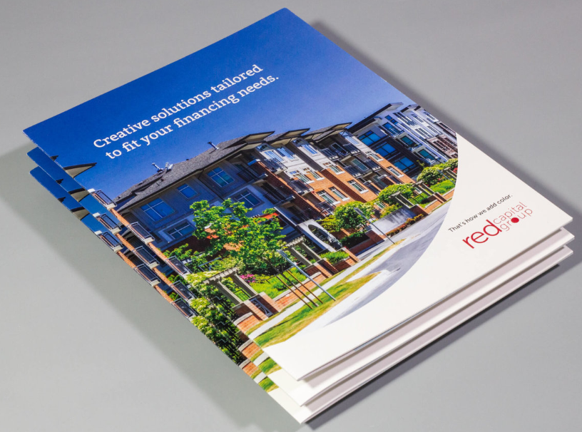 Stack of brochures with a residential complex image and the Red Dot logo.