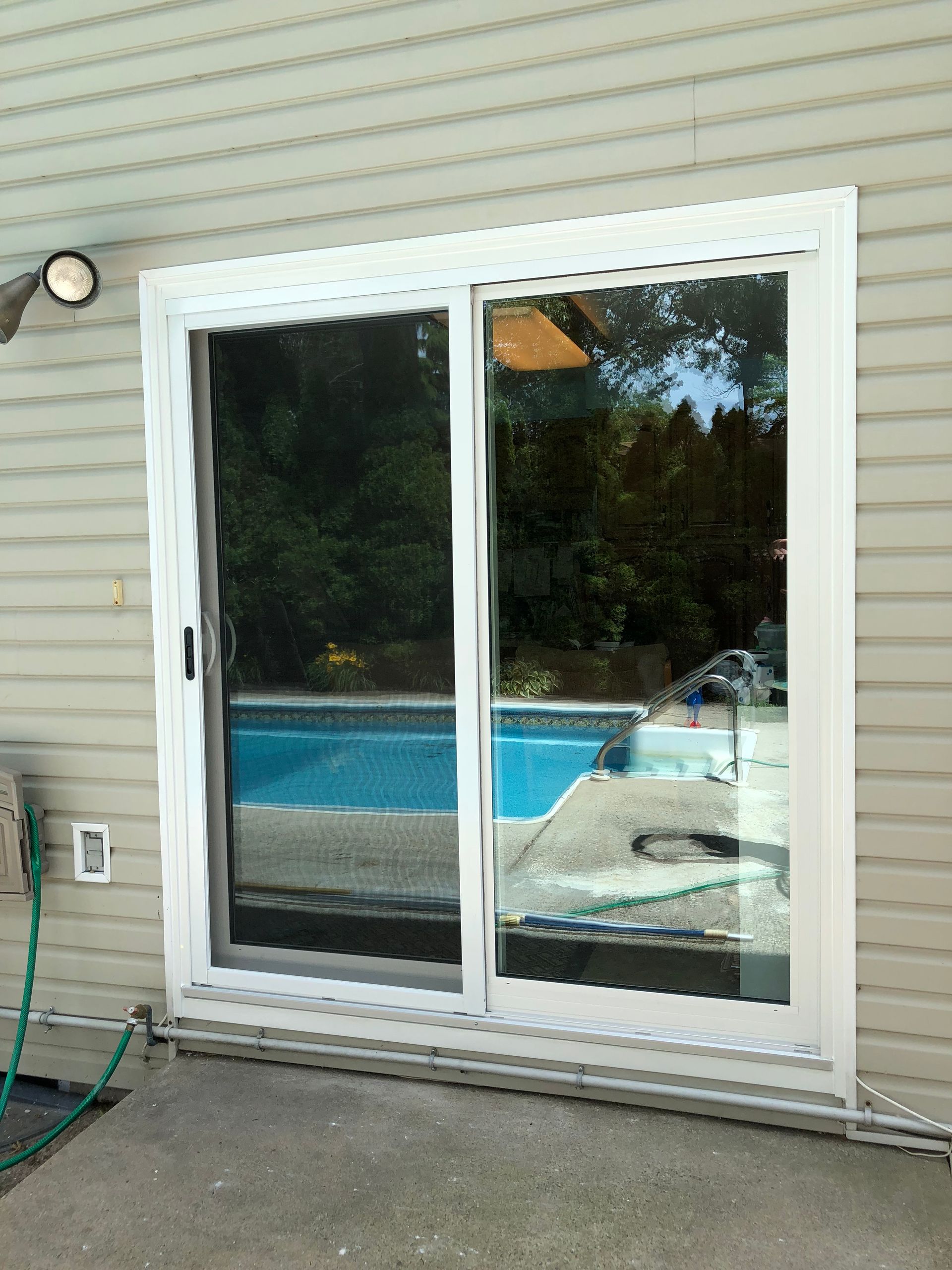 A sliding glass door with a view of a pool is on the side of a house.