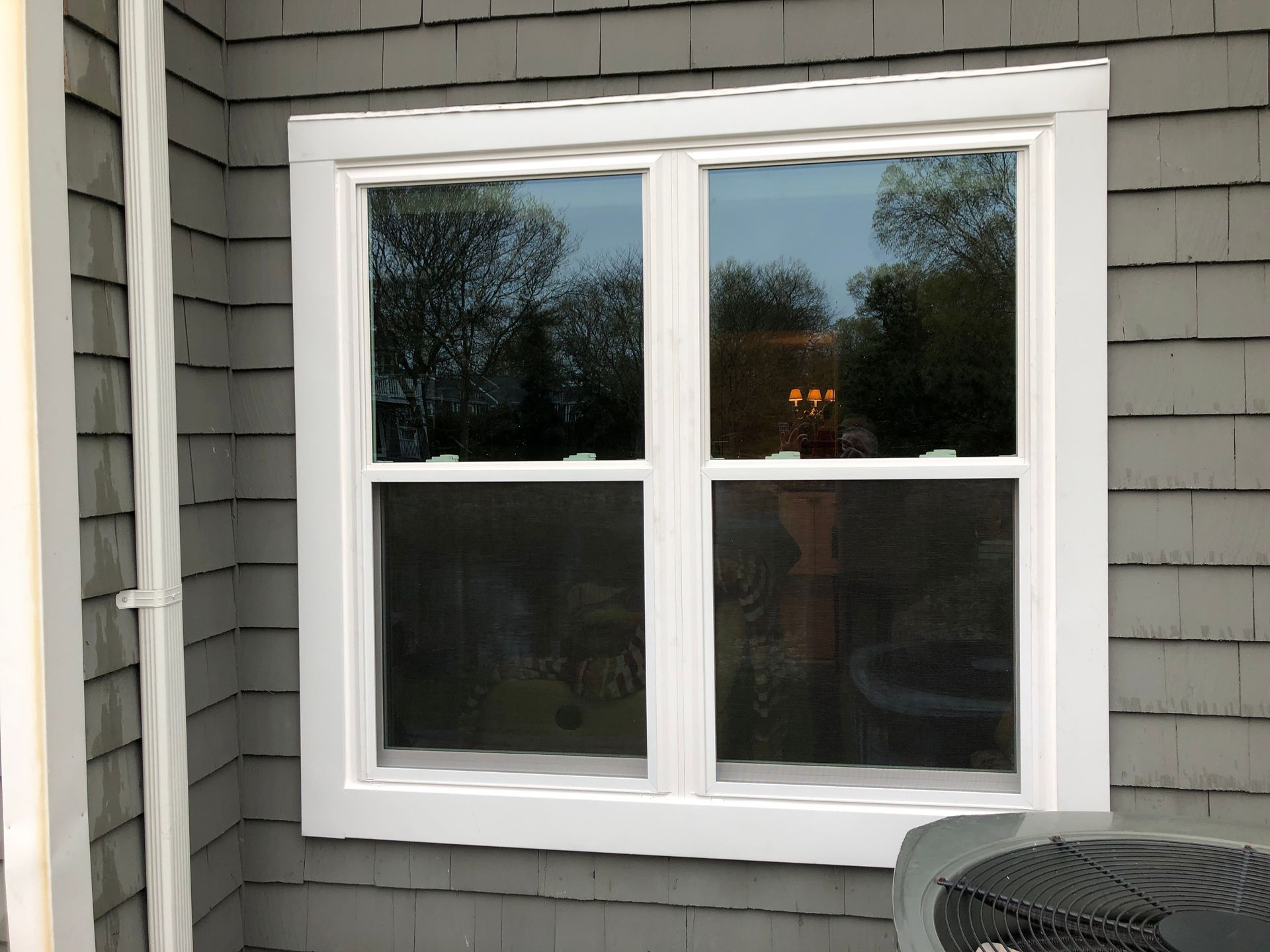 A white window is on the side of a house next to an air conditioner.