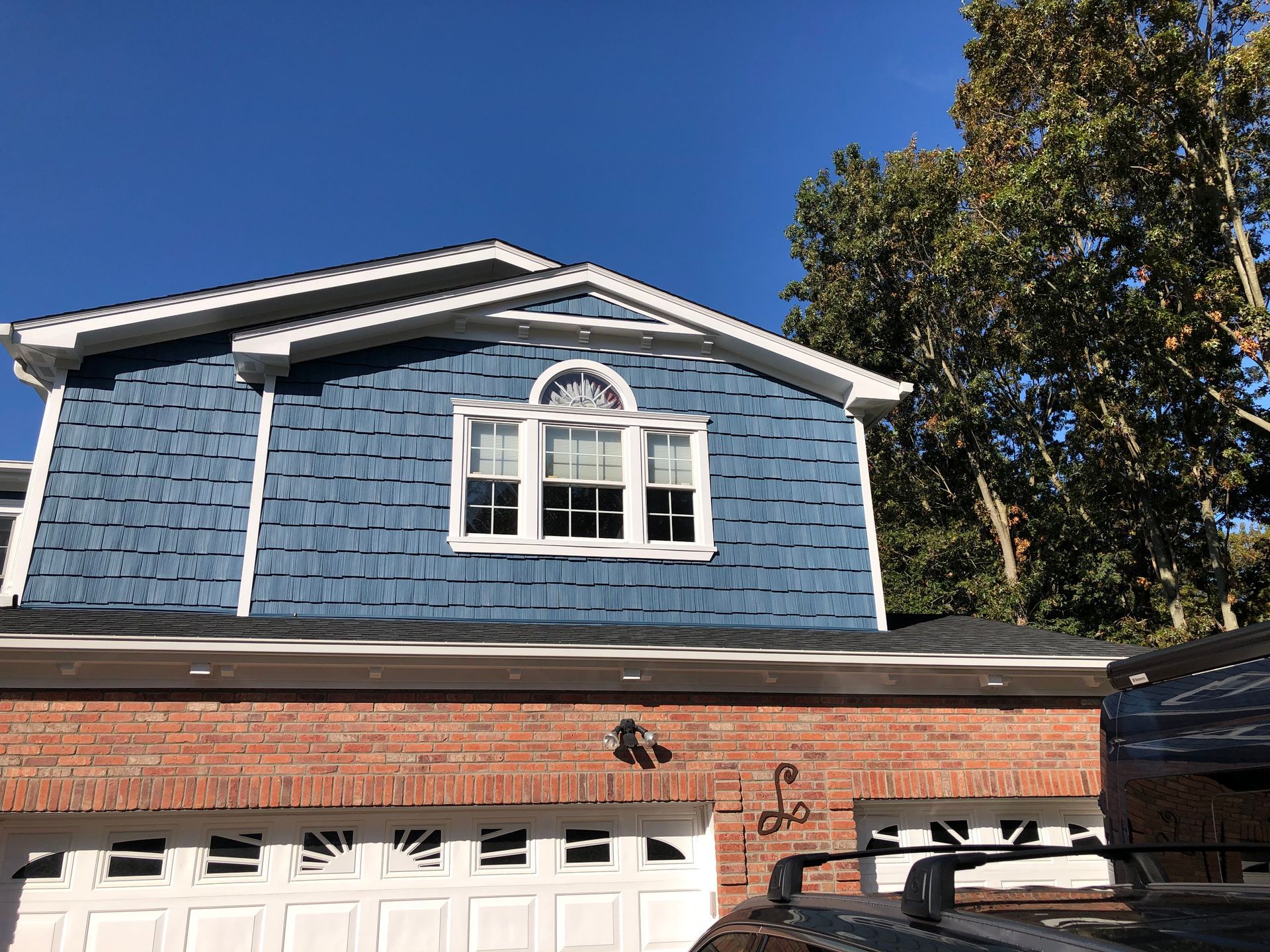 A blue house with a white window and a brick garage door.