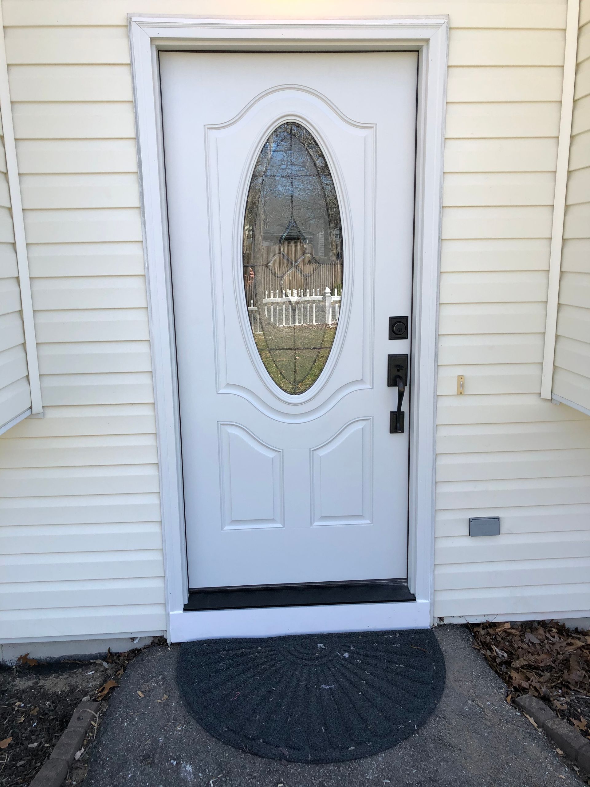 A white door with an oval window is sitting on a sidewalk.