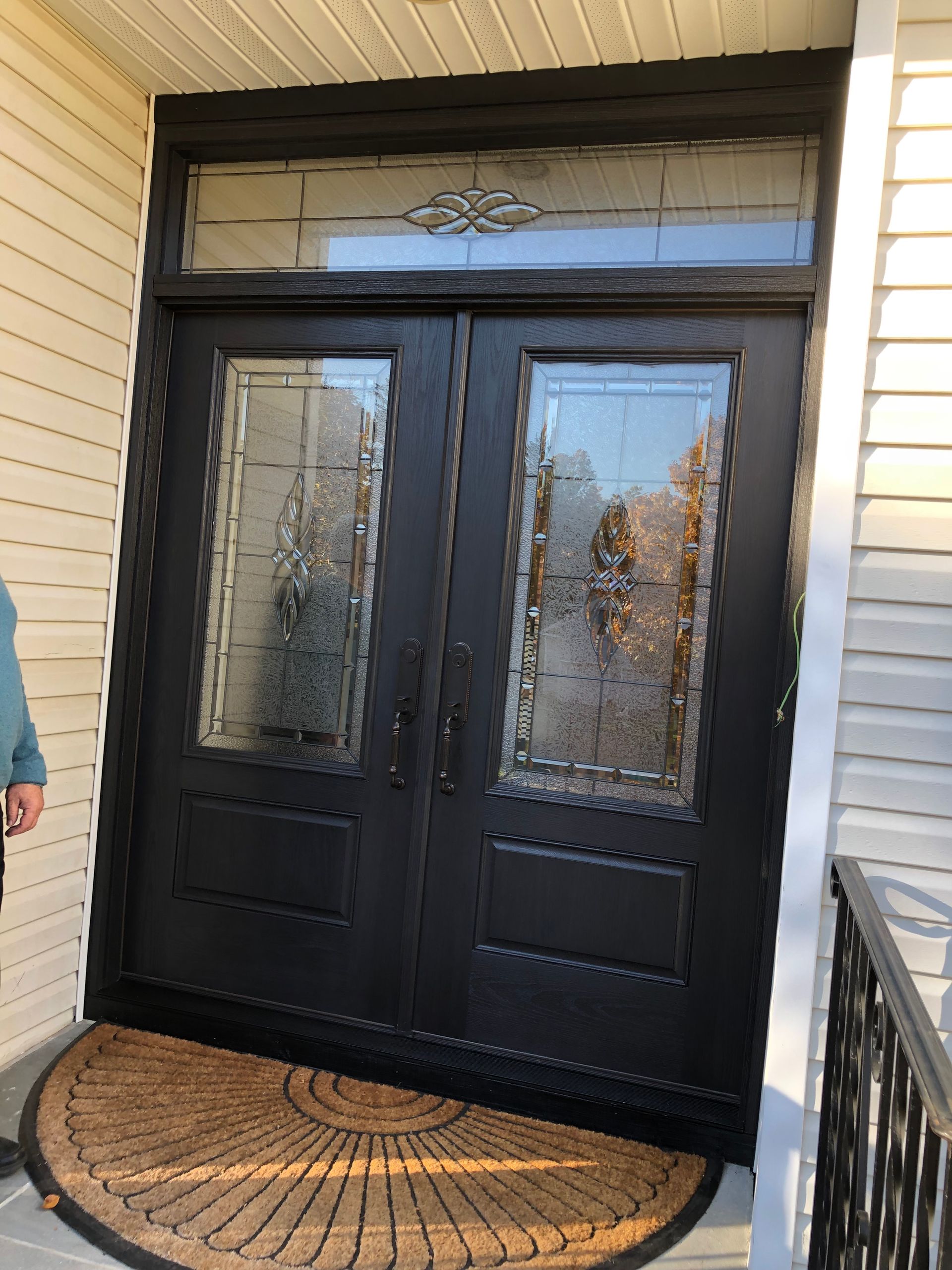 A man is standing in front of a black door with stained glass windows.