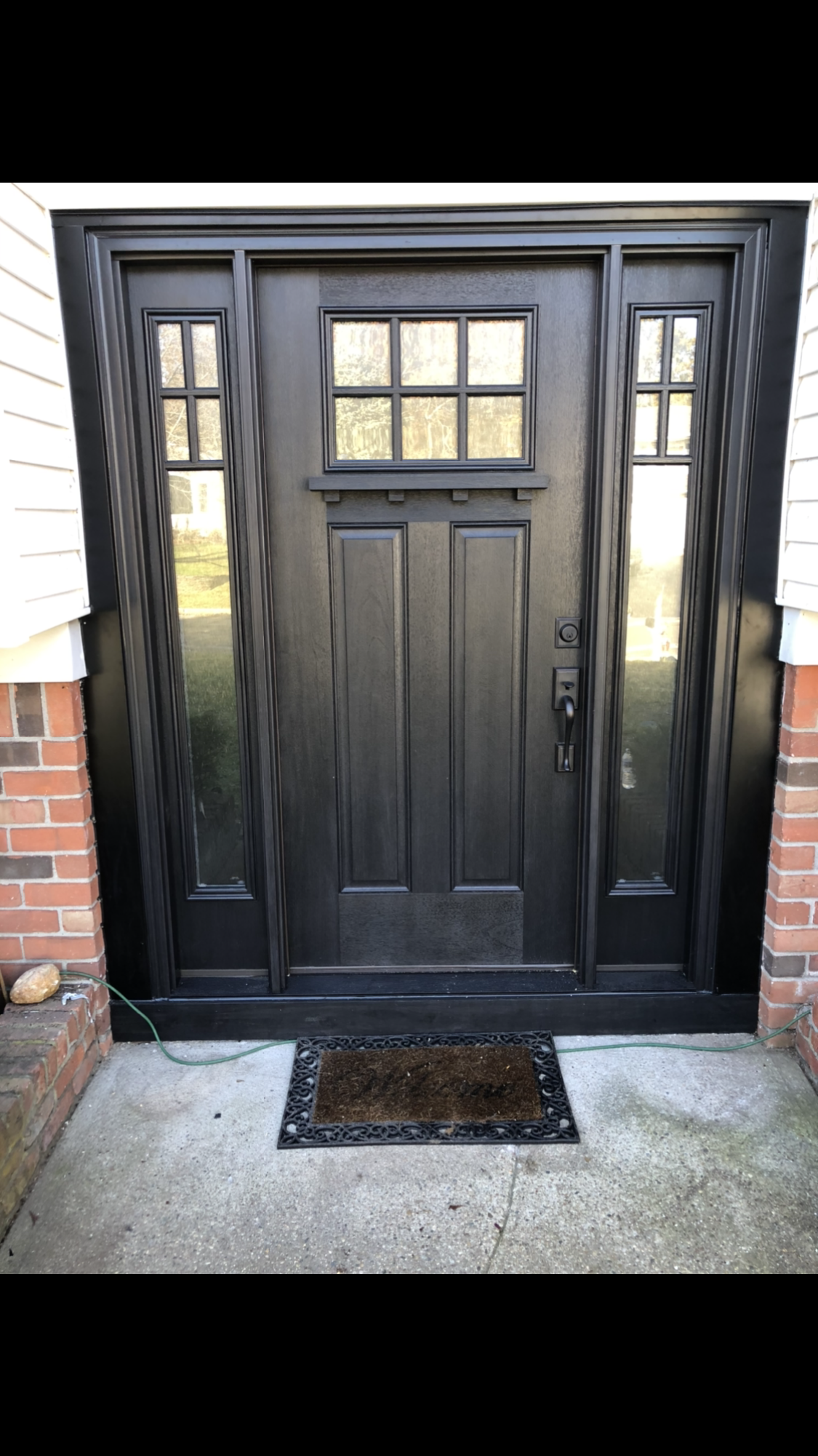 A black door is sitting on a concrete porch next to a brick wall.
