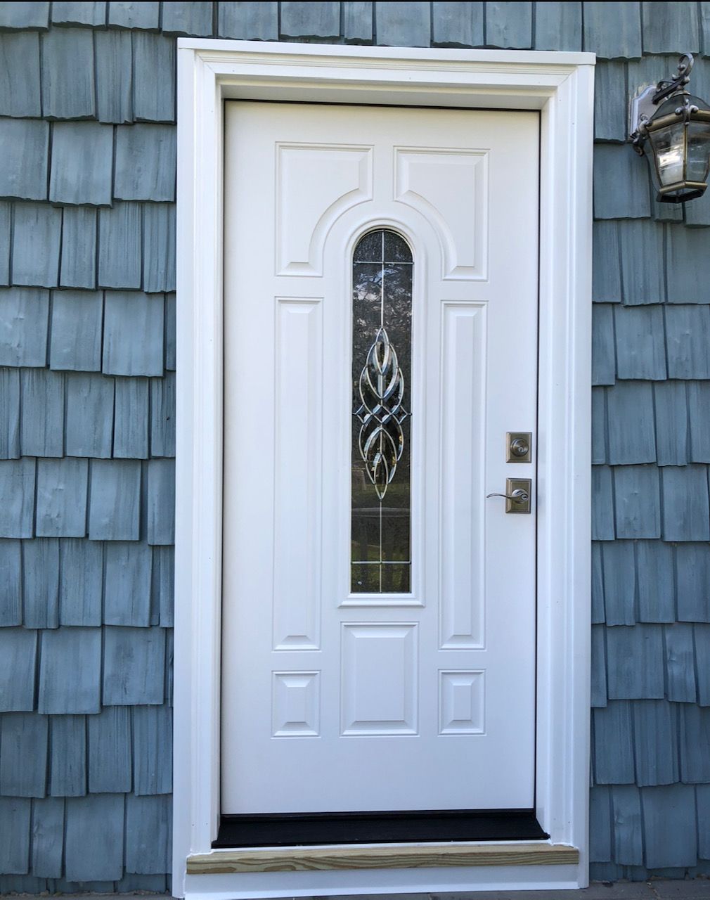 A white door with a stained glass window is on a blue house