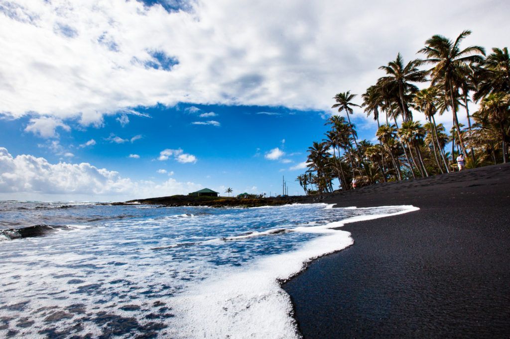 A black sandy beach with palm trees in the background