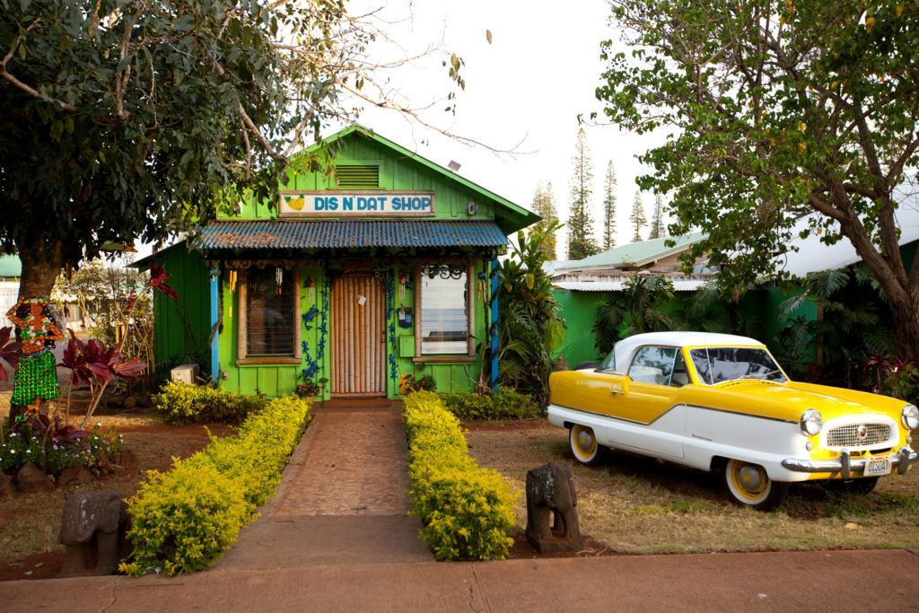 A yellow and white car is parked in front of a green house