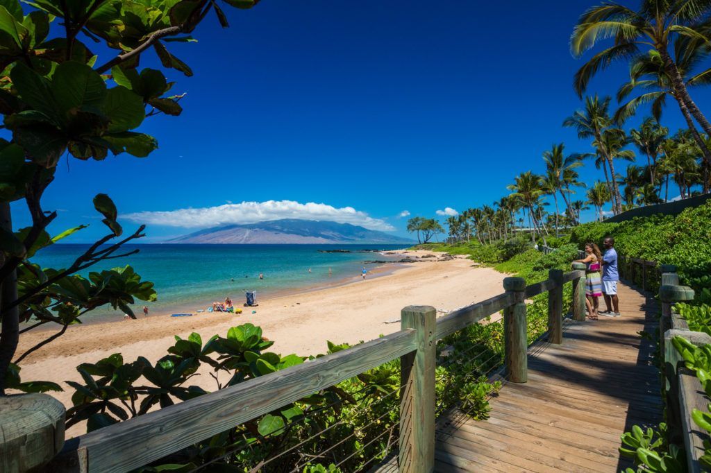 A wooden walkway leading to a beach with a mountain in the background.