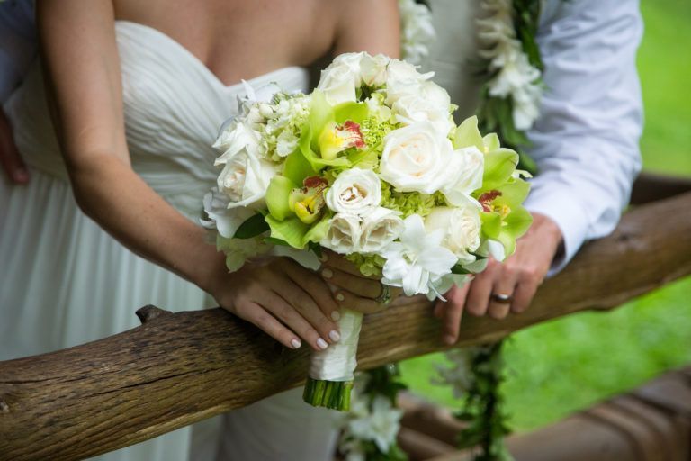 A bride and groom holding a bouquet of flowers on a wooden railing.