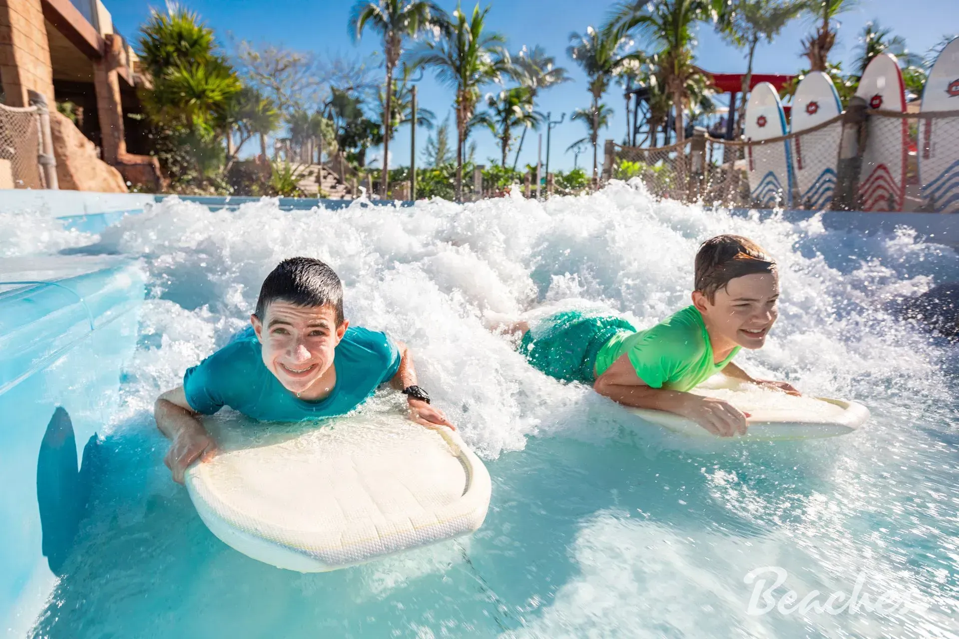 Two young boys are surfing in a wave pool at a water park.