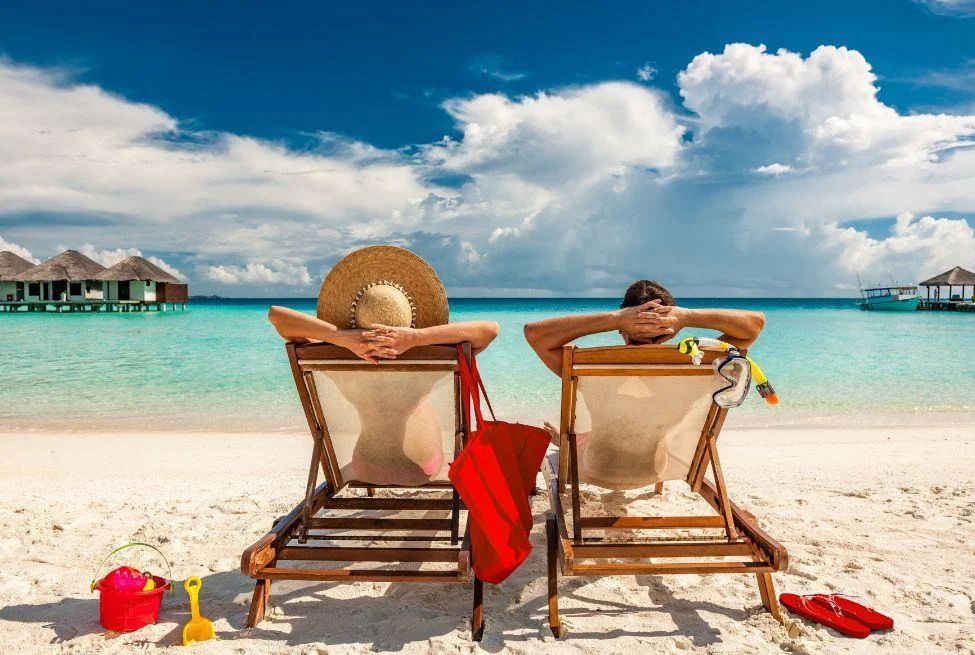 A man and a woman are sitting in lawn chairs on a beach.