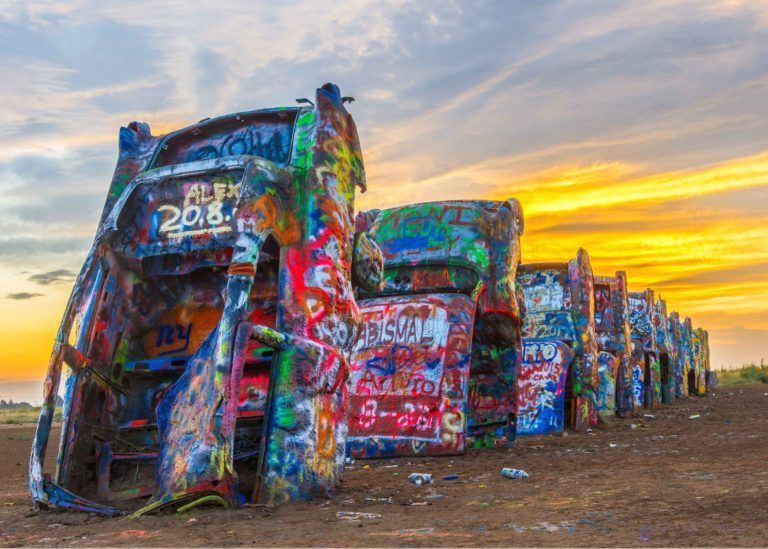 A row of cars are covered in graffiti at sunset.