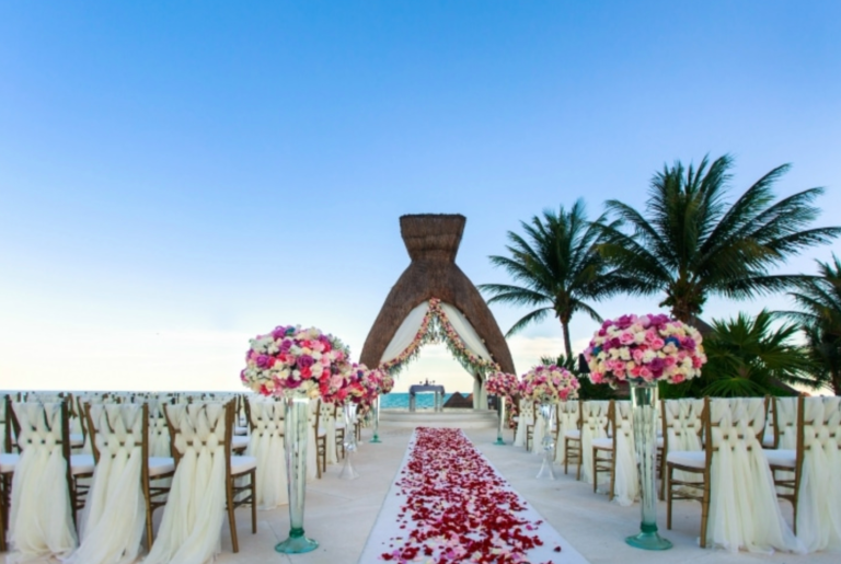 A wedding ceremony is set up on the beach with chairs and flowers