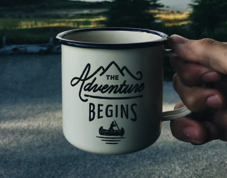 A person is holding a mug that says the adventure begins