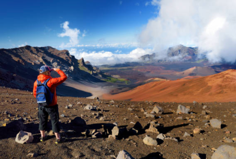 A person is standing on top of a mountain looking at the view.