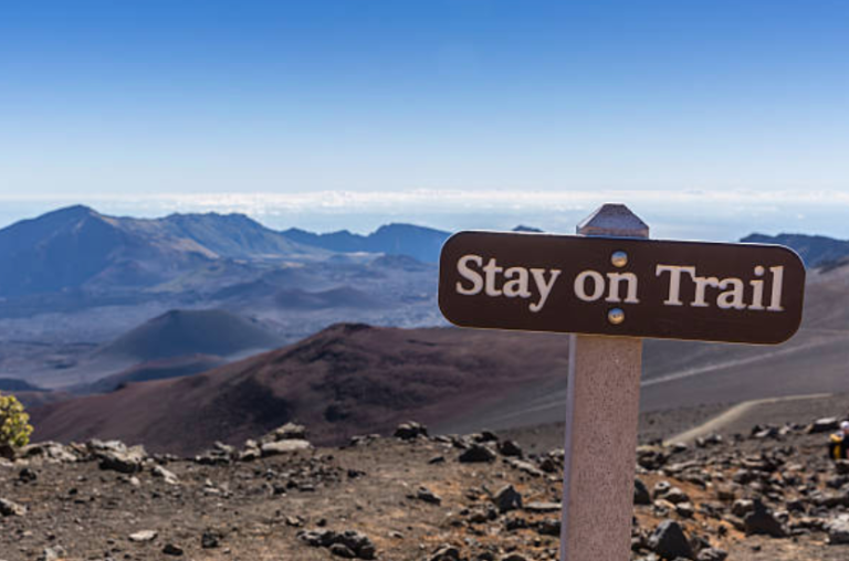 A sign that says `` stay on trail '' on top of a mountain.