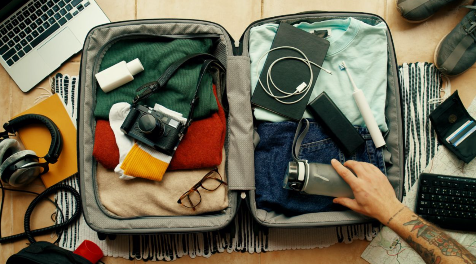 A person is packing a suitcase with clothes and a camera.