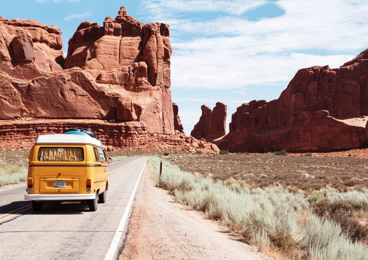 A yellow van is driving down a desert road.