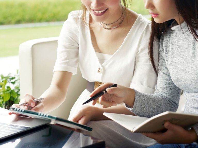 Two women are sitting on a couch looking at a tablet