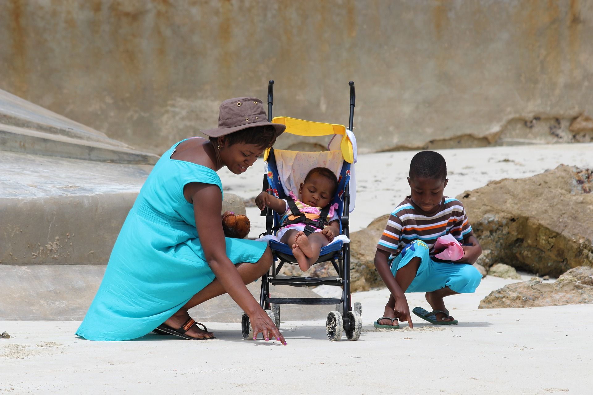 A woman is kneeling next to a stroller with a baby in it