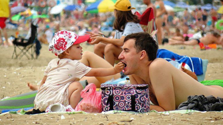 A little girl is feeding a man on the beach.