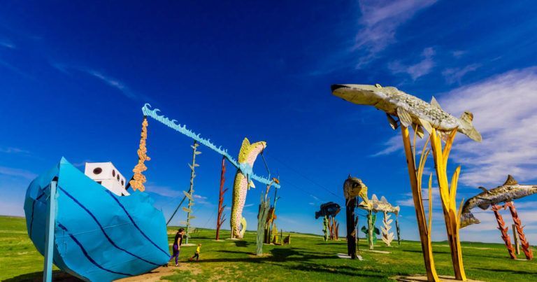 A group of sculptures in a field with a blue boat in the middle.