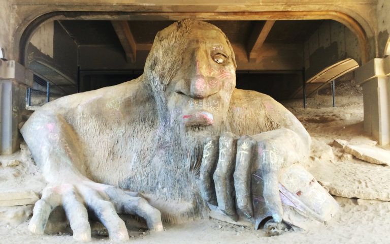 A statue of a man with a beard is laying in the dirt under a bridge.