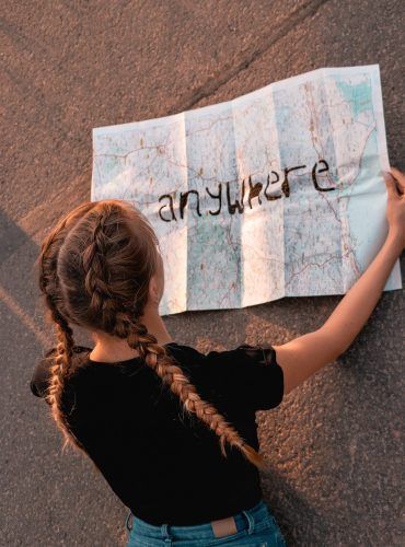 A girl is holding a map with the words `` anywhere '' written on it.