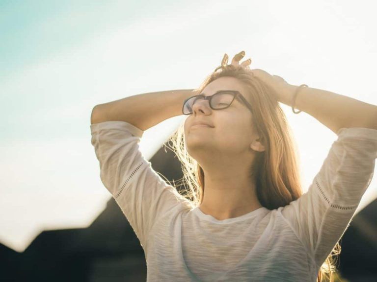 A woman wearing glasses and a white shirt is looking up at the sun.