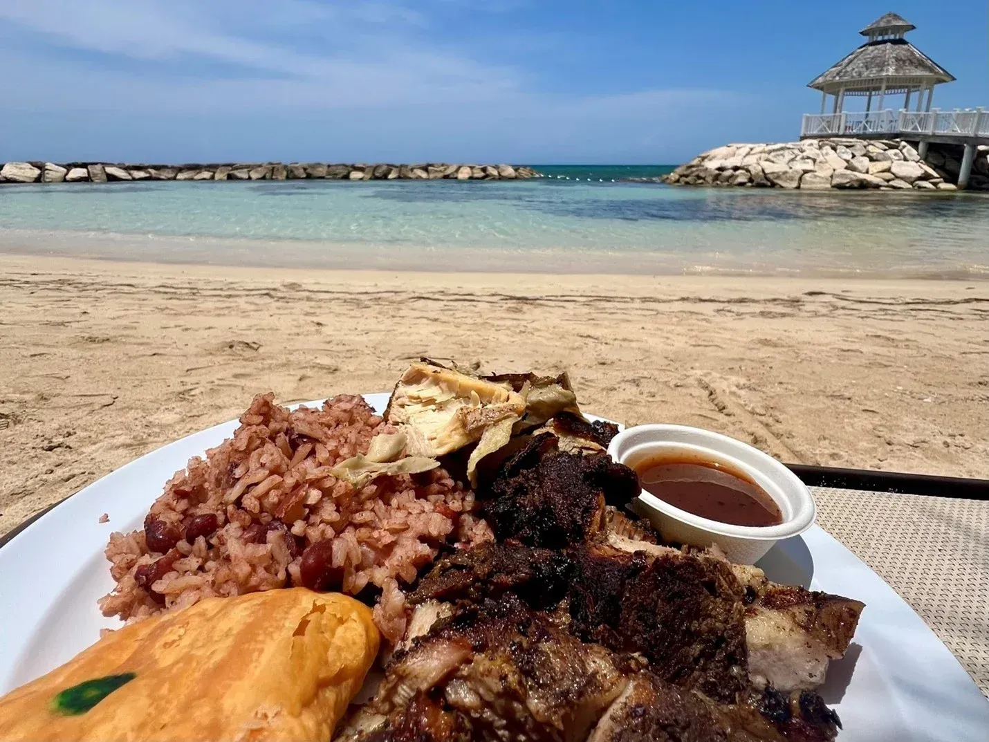 A plate of food on the beach with a gazebo in the background