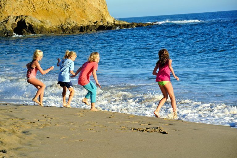 A group of young girls are running towards the ocean on a beach.