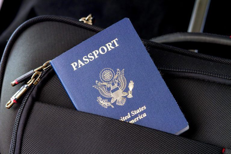 A blue passport is sitting on top of a black suitcase