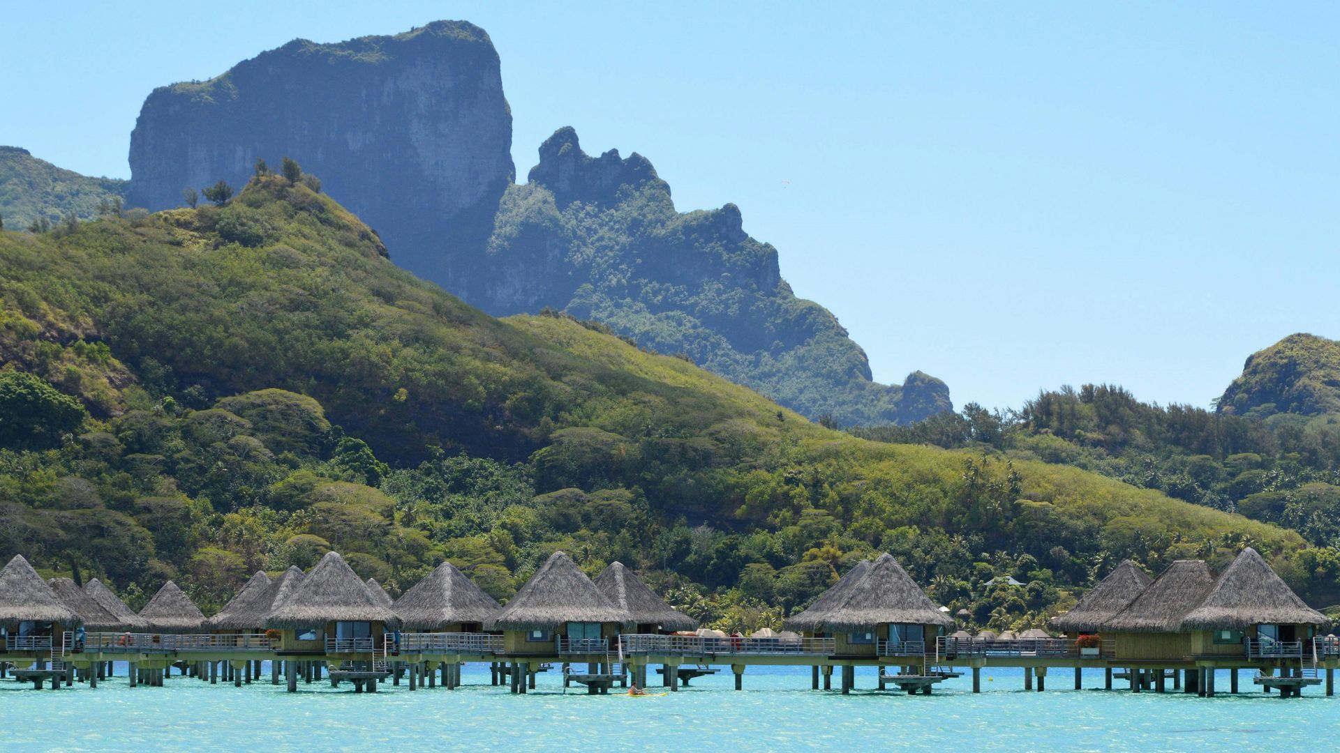 A row of bungalows in the water with a mountain in the background