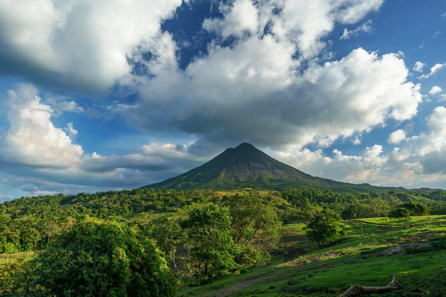 A mountain surrounded by trees and clouds on a sunny day.