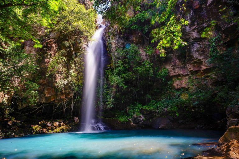 A waterfall is surrounded by trees and a blue lake.