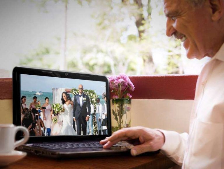 A man is using a laptop with a picture of a bride and groom on the screen.