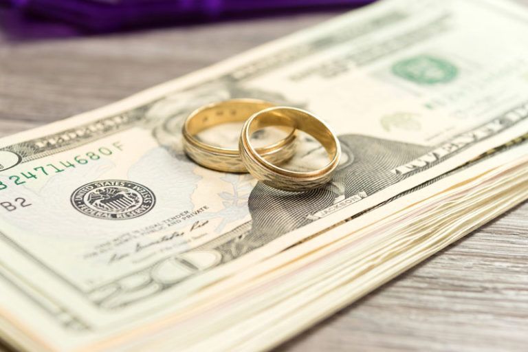 Two wedding rings are sitting on top of a stack of money.