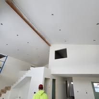 A man in a neon yellow hoodie is standing in a large room with a staircase.
