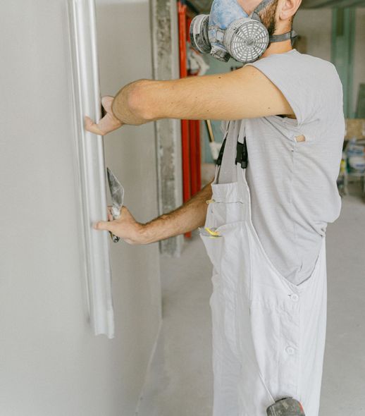 A man wearing a mask is plastering a wall.