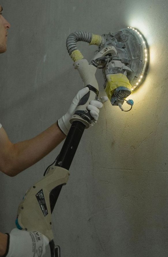 A person is using a sander on a wall with a light on it.